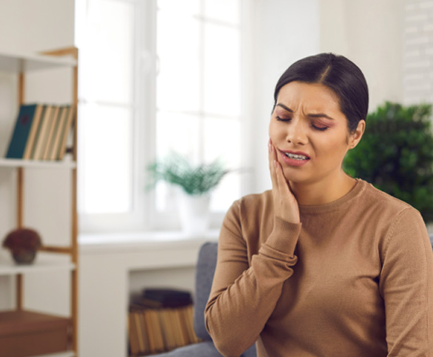 Woman sitting in chair rubbing jaw in pain