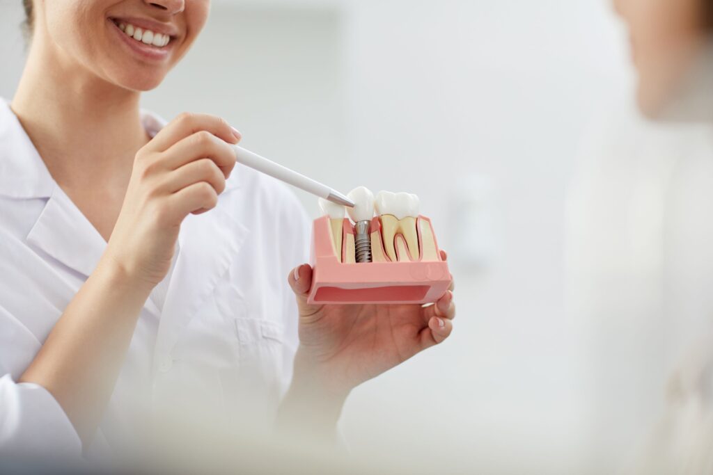 Nose-down view of dentist in white coat pointing to sample implant with pen